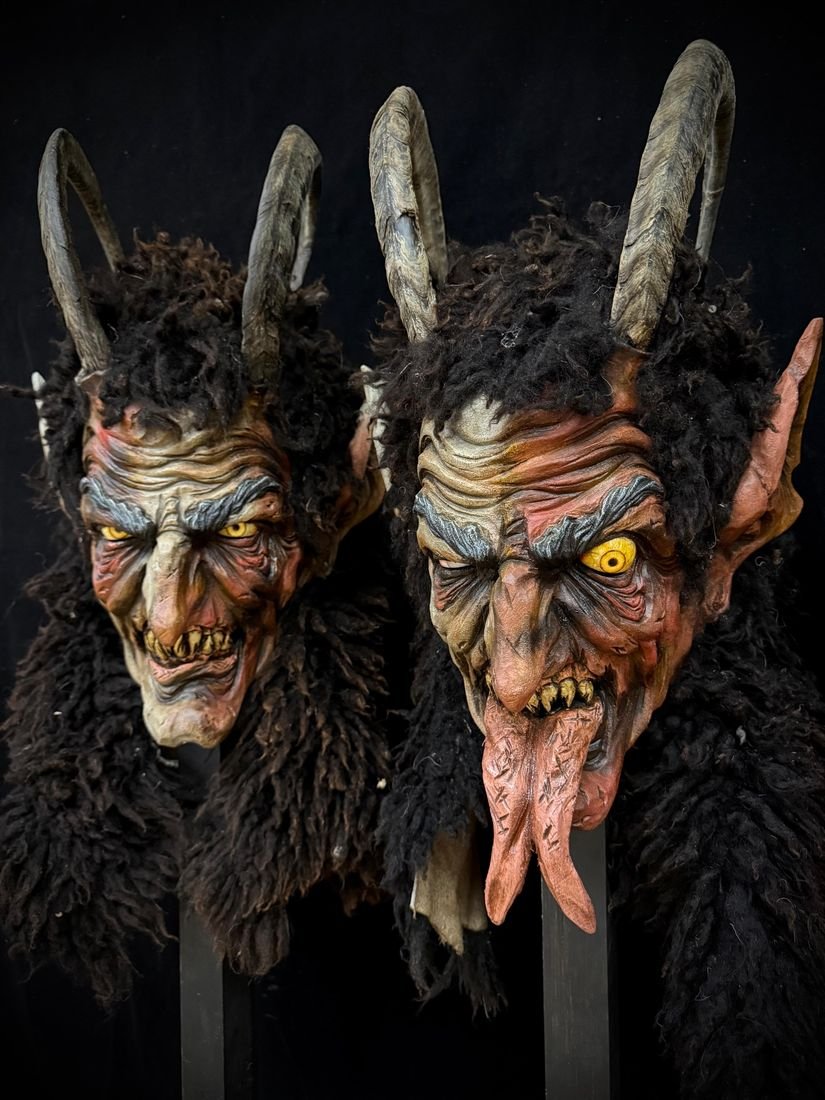 Zwei Krampusmasken mit dunklem Fell, gelben Augen und langer Zunge