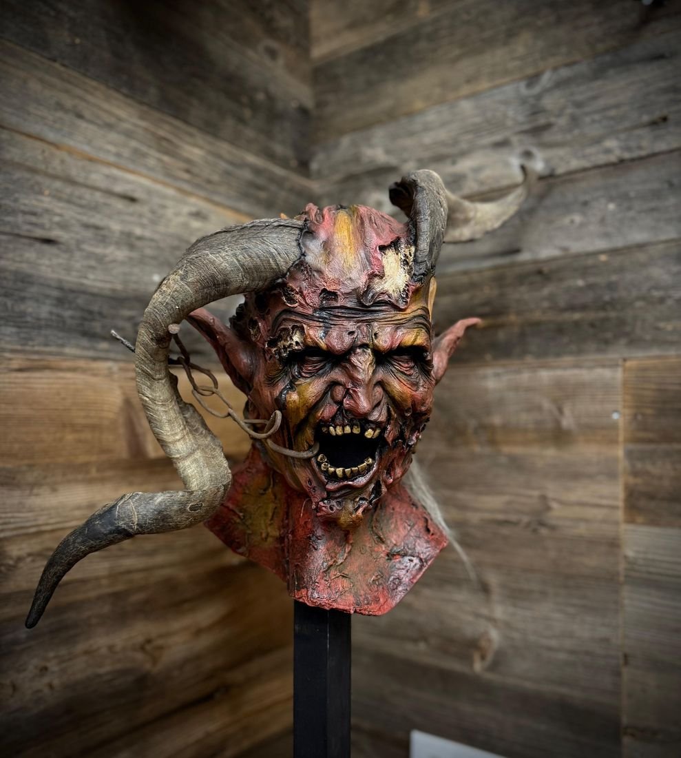 Rot bemalte Maske mit offenem Mund vor Holzwand