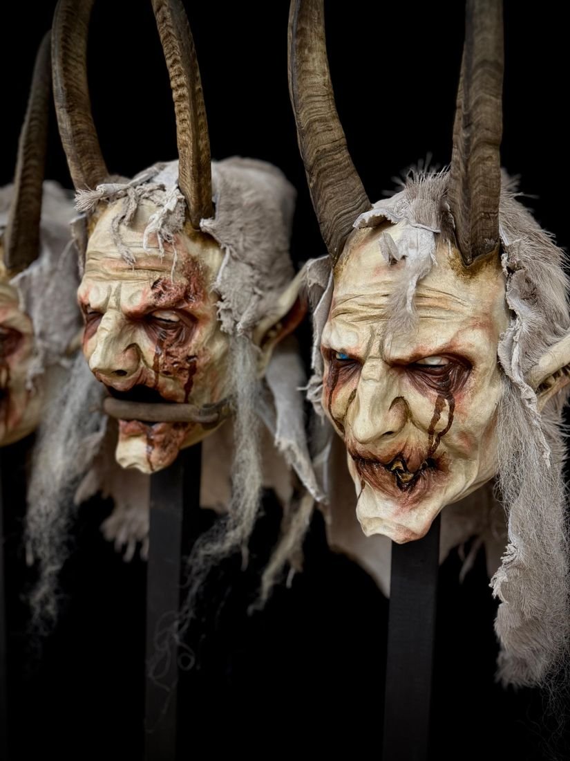 Zwei blasse Masken mit Fellhauben, Hörnern und blutigen Augen